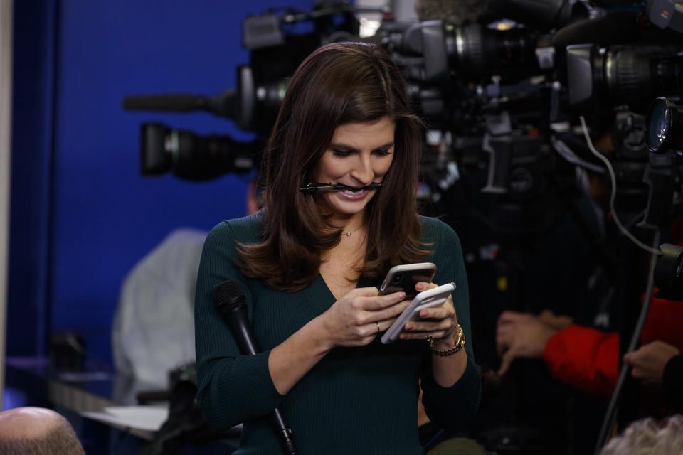 Kaitlan Collins checks her phone while holding a pen in her teeth.