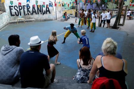 A member of the Acorda Capoeira (Awaken Capoeira) group teaches capoeira to two foreign visitors in the Rocinha favela in Rio de Janeiro, Brazil, July 26, 2016. REUTERS/Bruno Kelly