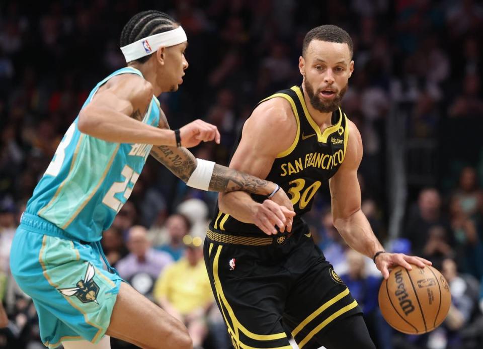 Golden State Warriors guard Steph Curry, right, begins to drive around Charlotte Hornets guard Tre Mann, left, during first quarter action at Spectrum Center in Charlotte, NC on Friday, March 29, 2024.