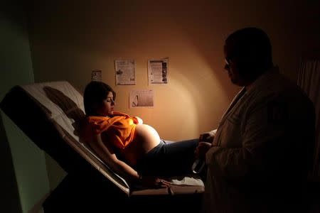 Noriany Rivera, who is 40 weeks pregnant, looks at her belly as she listens to a doctor during a routine check up, as flyers explaining how to prevent Zika, Dengue and Chikungunya viruses are posted on the wall, at a public hospital in San Juan, Puerto Rico, February 3, 2016. REUTERS/Alvin Baez/File Photo