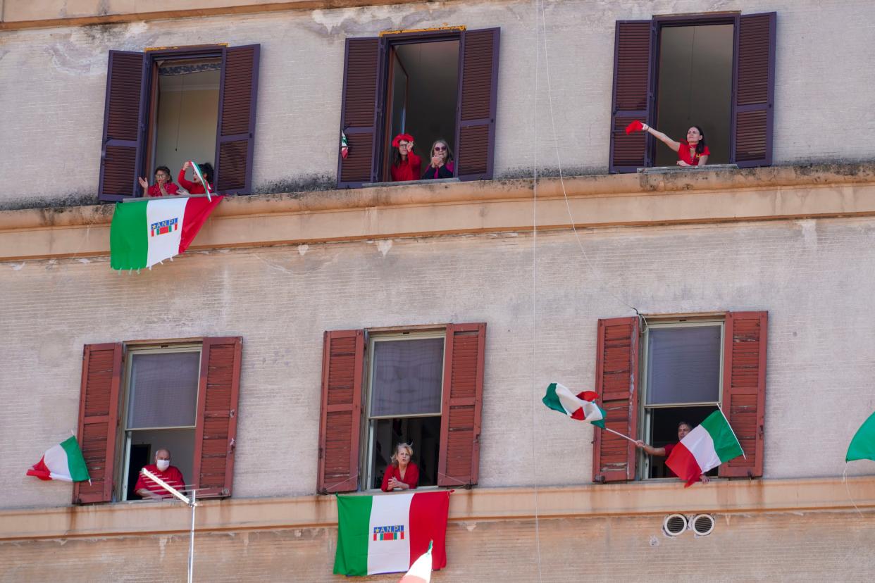 People wave and chant from their windows with Italian flags draped on the occasion of the 75th anniversary of Italy's Liberation Day in Rome, Italy on Saturday, April 25, 2020. Italy's annual commemoration of its liberation from Nazi occupation is celebrated on April 25, but lockdown measures in the coronavirus-afflicted country mean no marches can be held this year and the National Association of Italian Partisans has invited all to sing “Bella Ciao," the anthem of Italy’s communist resistance, from their windows.