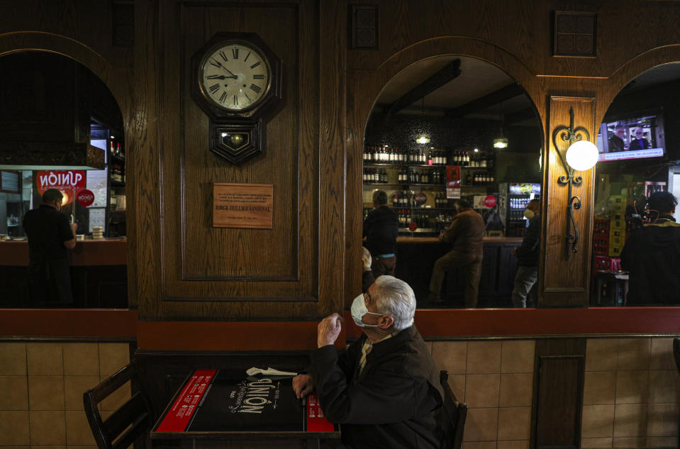 A customer wearing a mask to curb the spread of the new coronavirus, stands by for a waiter at La Union bar in Santiago, Chile, Monday, July 19, 2021. Santiago is moving into Phase 3, ending with the weekend quarantines and allowing more people inside restaurants and gyms as the city relaxes its lockdown rules. (AP Photo/Esteban Felix)