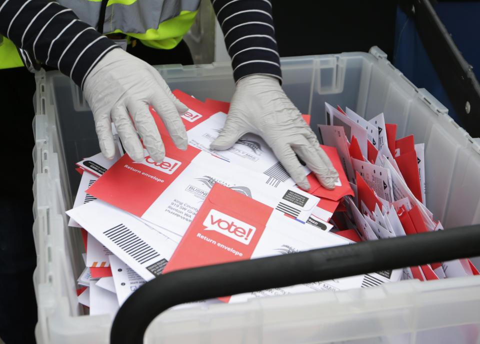 FILE - In this March 10, 2020, file photo wearing gloves, a King County Election worker collect ballots from a drop box in the Washington State primary, in Seattle. But the 2020 presidential election is creeping ever closer, and there are no signs yet of pandemic abating, nor any word on when Americans on orders to stay home can resume normal life, and so lawmakers are trying to figure how to allow for voting in a world where face-to-face contact causes anxiety at the least, and sickness and death at the most. (AP Photo/John Froschauer, File)