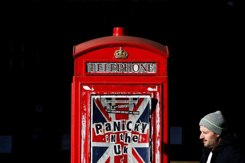 FILE PHOTO: A pedestrian walks past an advertisement for 'Panicky in the UK' displayed on a phone box in the Soho district after they closed because of the spread of coronavirus disease (COVID-19), in London