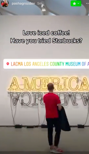 Pavel looking at a neon sign that says America at a museum with the caption "Love iced coffee! Have you tried Starbucks?"