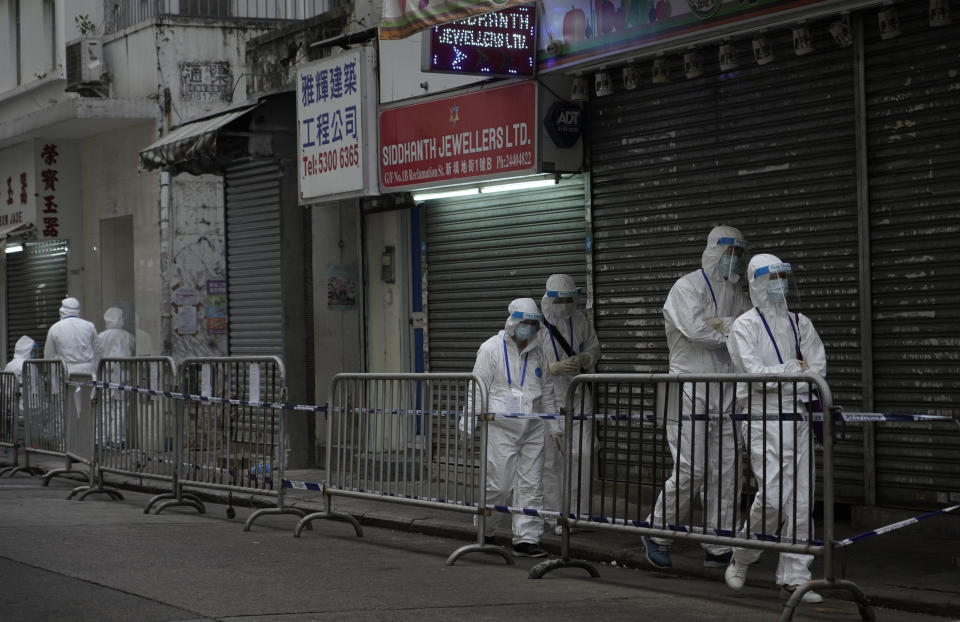 Government workers wearing personal protective equipment walk at the closed area in Jordan district, in Hong Kong, Sunday, Jan. 24, 2021. Thousands of Hong Kong residents were locked down Saturday in an unprecedented move to contain a worsening outbreak in the city, authorities said. (AP Photo/Vincent Yu)