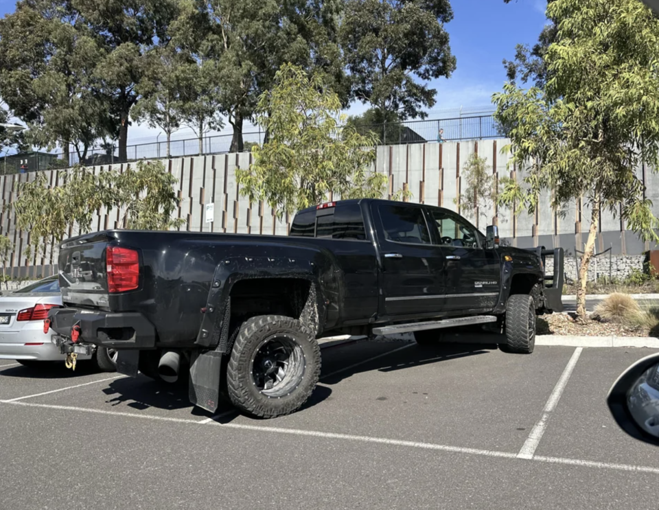 A large black GMC truck pictured parked diagonally across two spots in a Melbourne shopping centre car park.