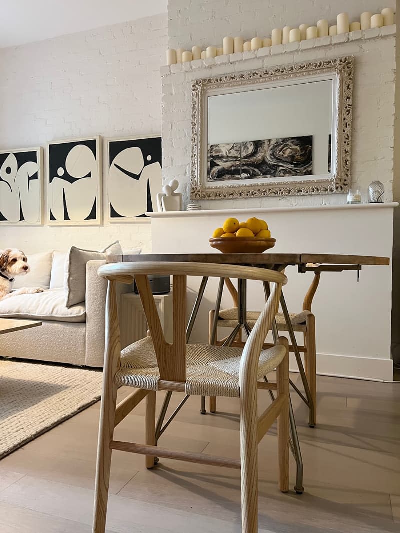 Round Eiffel Tower base table and woven chairs in dining area with candles over mirror hung on neutral wall.