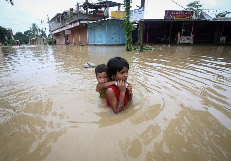 FILE PHOTO: A girl carries her brother as she wades through a flooded road after heavy rains on the outskirts of Agartala