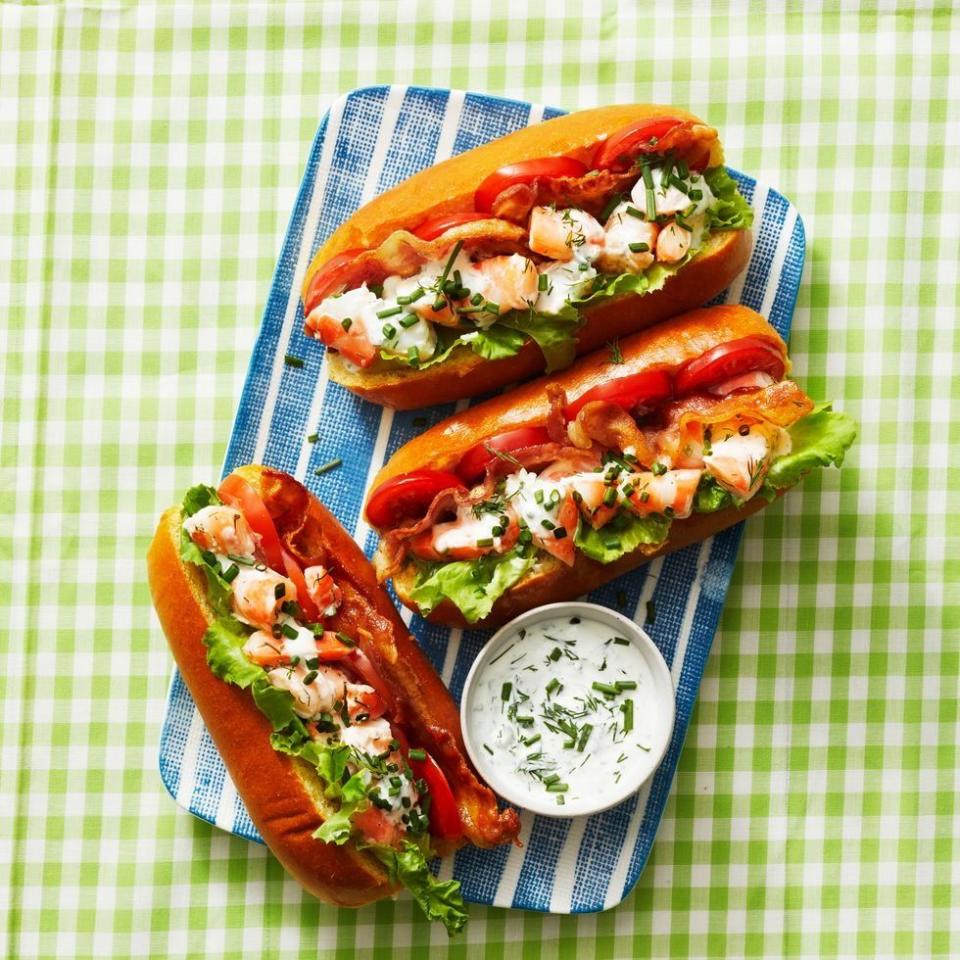 three shrimp rolls in hot dog buns with a side of creamy dip