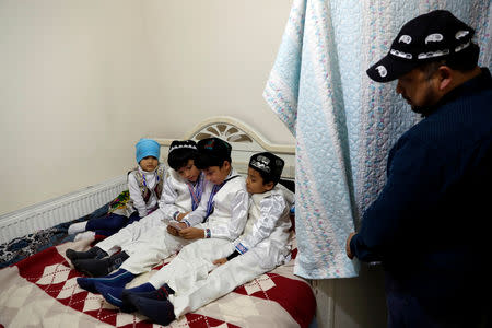 Qurbanjan Nourmuhammed looks on as his children play a game on a mobile phone at their home in Istanbul, Turkey, December 12, 2018. REUTERS/Murad Sezer