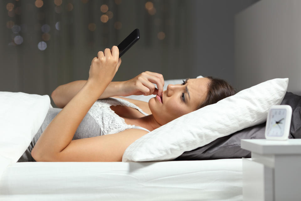 Nervous woman reading phone message on a bed in the night at home