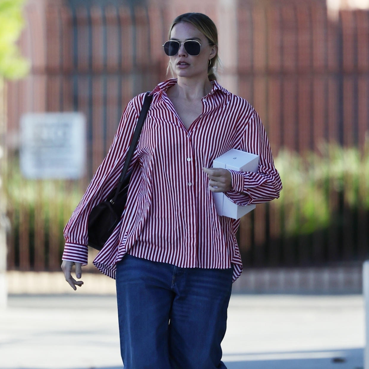  Margot Robbie wearing an oversized red and white button down with sunglasses and a black shoulder bag. 