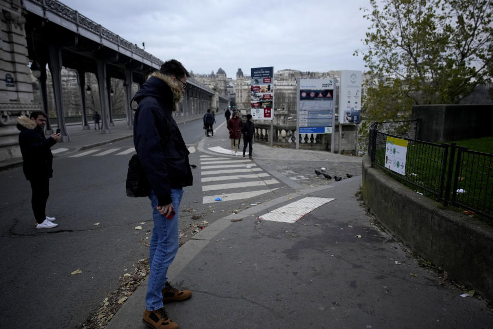 People look at a blood stain on the scene where a man targeted passersbys late saturday, killing a German tourist with a knife and injuring two others in Paris, Sunday, Dec. 3, 2023. (AP Photo/Christophe Ena)