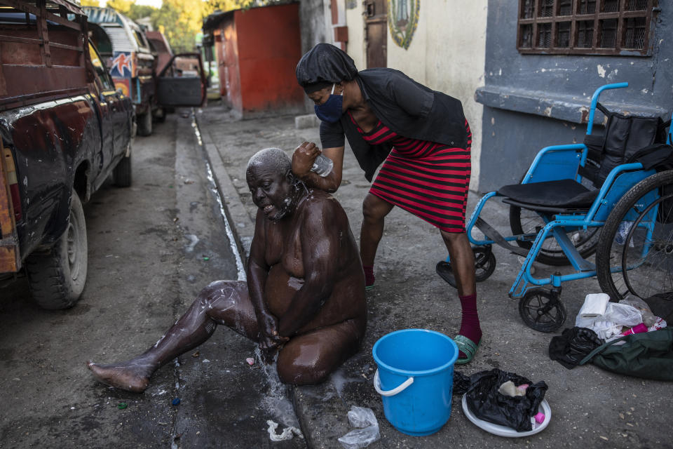 Marie Joseph bathes her friend Jean Robert outside a shelter for the internally displaced where they live due to police violence in Port-au-Prince, Haiti, Thursday, Sept. 16, 2021. Most of the population of Port-au-Prince has no access to basic public services, no drinking water, electricity or garbage collection. (AP Photo/Rodrigo Abd)