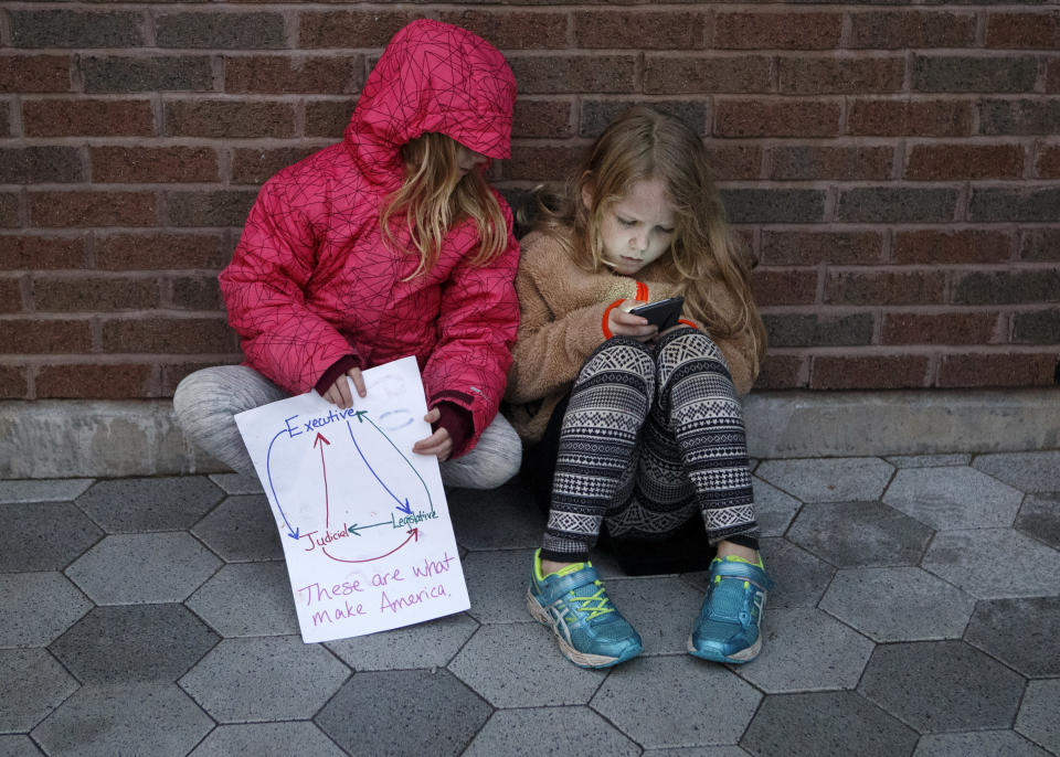 Seven-year-old Audrey Lucas, left, holds a sign showing the branches of the government as she looks at the phone her 9-year-old sister Addie is holding during a MoveOn "Nobody is Above the Law" protest at Miller Park on Thursday, Nov. 8, 2018 in Chattanooga, Tenn. The protestors gathered to voice objections to President Trump's appointment of Matt Whitaker as acting attorney general. (C.B. Schmelter/Chattanooga Times Free Press via AP)