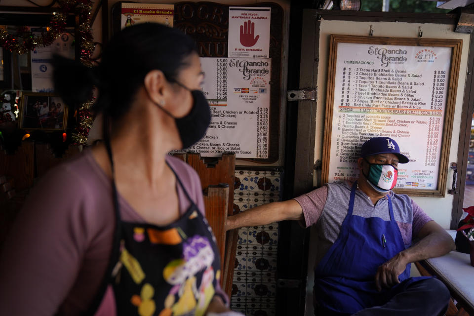 Debbie Briano, foreground, a fourth-generation owner of Mexican restaurant, El Rancho Grande, talks to her cook Valo Martinez while waiting for customers on empty Olvera Street in downtown Los Angeles, Wednesday, Dec. 16, 2020. Even as the December light casts long shadows over the market, Briano is not giving up. She's serving takeout food and is paying five employees, including brothers who have worked there 55 years and 48 years each, but not herself. (AP Photo/Jae C. Hong)