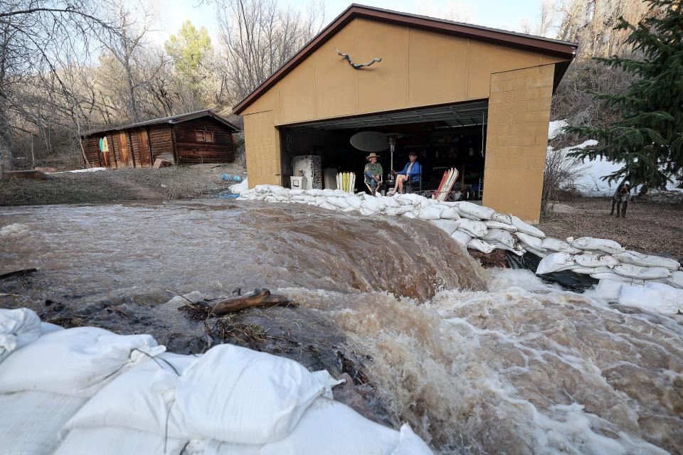 Miguel Jimenez and Andy McNeil chat in McNeil’s garage as water from snowmelt rushes past them on Killyons Lane in Emigration Canyon on Tuesday, May 2, 2023. | Kristin Murphy, Deseret News