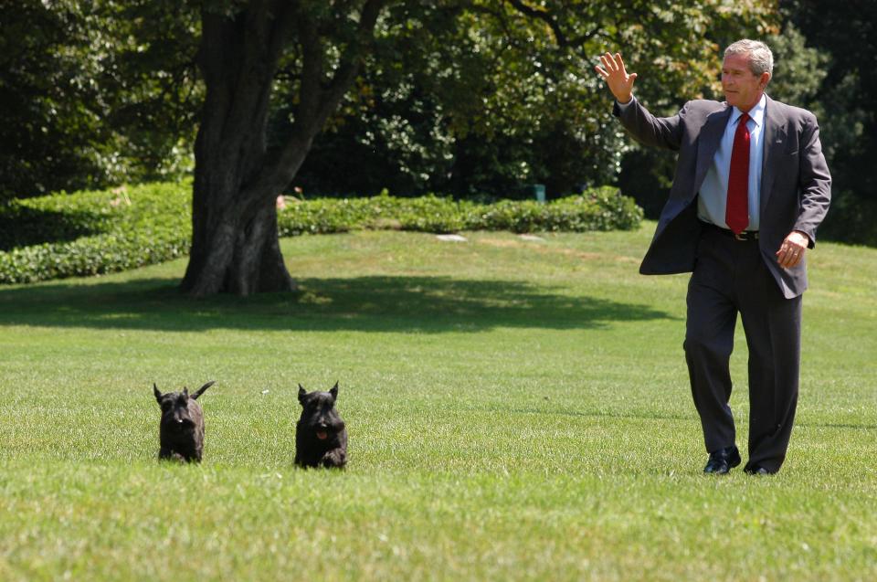 President George W. Bush waves as he arrives on the South Lawn of the White House with his dogs, Barney and Miss Beazley, in 2006.