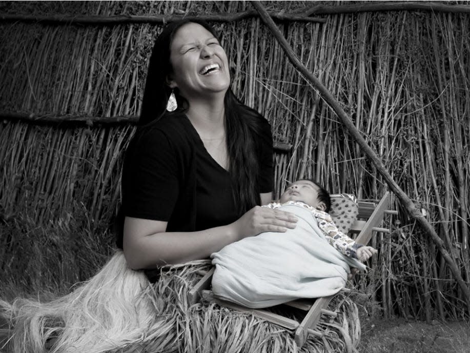 A Native American woman laughs while holding her baby.