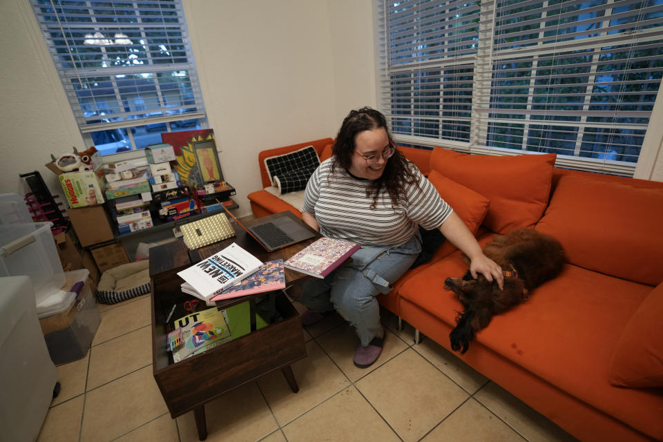 Krystal Guerra, 32, pauses to pet her dog Einstein as she does online coursework for a degree program in digital marketing, inside the apartment which she is packing up to leave after her new landlord gave her less than a month's notice that her rent would go up by 26%, Saturday, Feb. 12, 2022, in the Coral Way neighborhood of Miami. Guerra, who works in marketing while also pursuing a degree part-time, had already been spending nearly 50% of her monthly income on rent prior to the increase. Unable to afford a comparable apartment in the area as rents throughout the city have risen dramatically, Guerra is putting many of her belongings into storage and moving in with her boyfriend and his daughter for the time being. (AP Photo/Rebecca Blackwell)