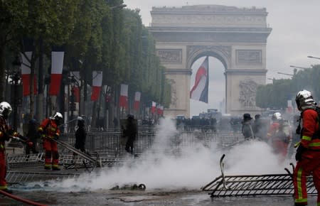 French firefighters extinguish a fire on the Champs Elysees avenue near the Arc de Triomphe during clashes with protesters after the traditional Bastille Day military parade in Paris