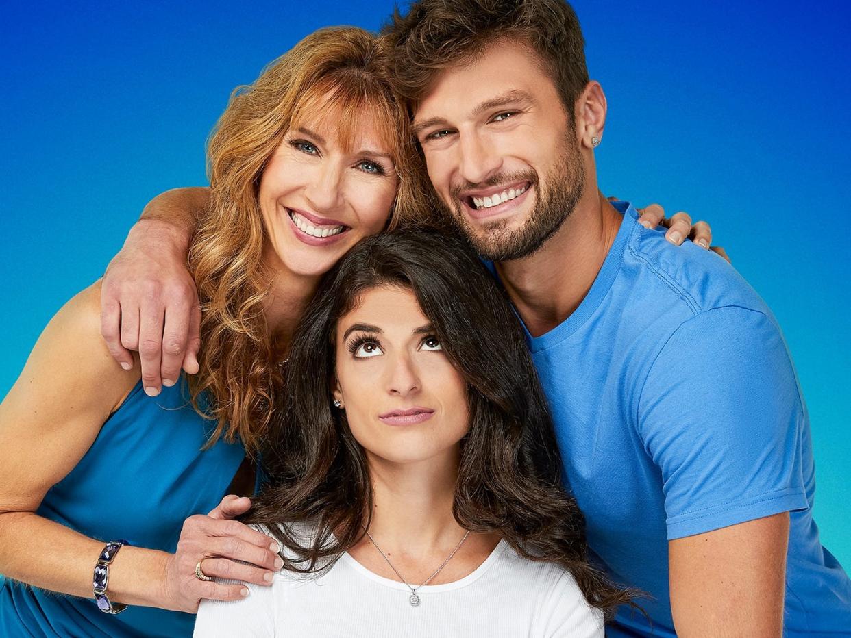 A mother and son embrace while the son's girlfriend looks up at them from below.