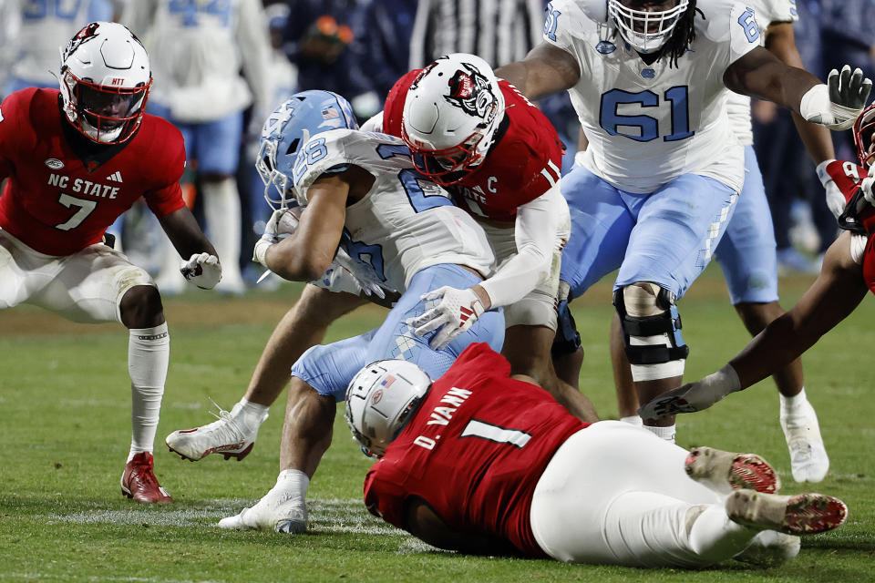 North Carolina running back Omarion Hampton (28) gets wrapped up by North Carolina State linebacker Payton Wilson (11) and defensive tackle Davin Vann (1) with cornerback Shyheim Battle (7) nearby during the second half of an NCAA college football game in Raleigh, N.C., Saturday, Nov. 25, 2023. (AP Photo/Karl B DeBlaker)