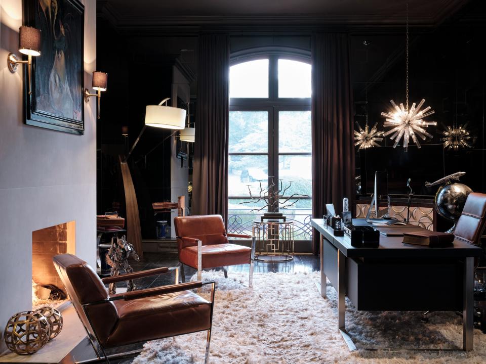 The mostly-black home office is more muted than other spaces in the home, which was intentional. A handful of outdoor street signs with inspirational names—“Ambition Way,” “Billionaire Boys Lane”—are visible from inside, and help get the creative juices flowing. The desk was sourced from Cantoni in L.A. The walls are covered in custom mirrors. The chandelier and other lighting come from Arteriors. The chairs are Bernhardt.