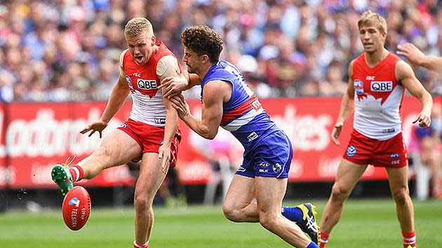 Daniel Hannebery of the Swans kicks whilst being tackled by Tom Liberatore of the Bulldogs. Pic: Getty