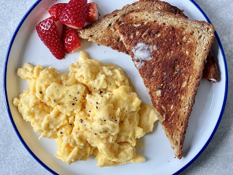 Scrambled eggs on plate with buttered toast and strawberries