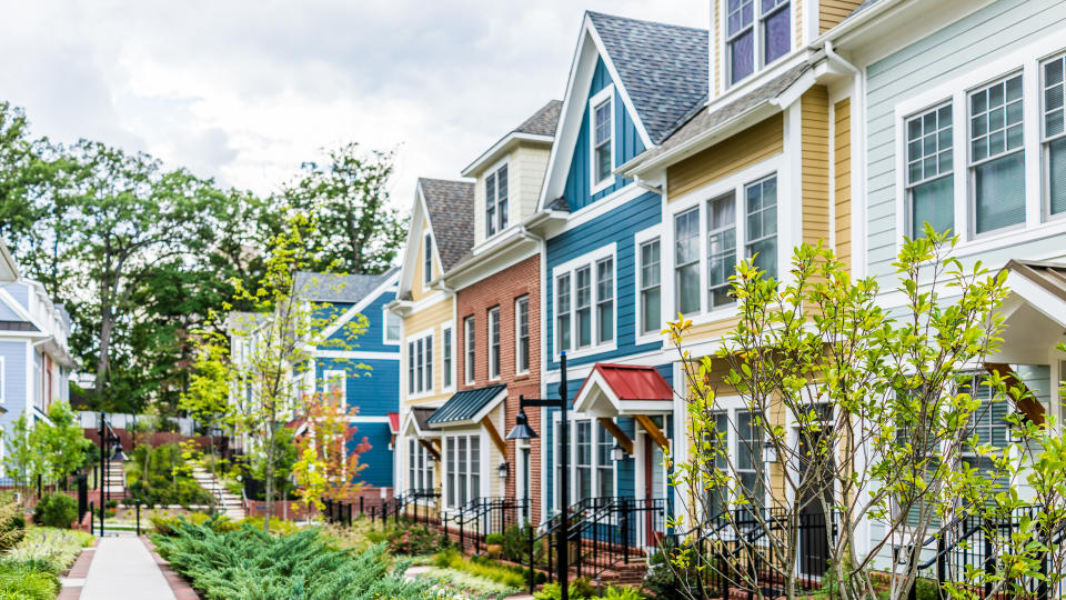 Row of colorful, red, yellow, blue, white, green painted residential townhouses, homes, houses with brick patio gardens in summer.