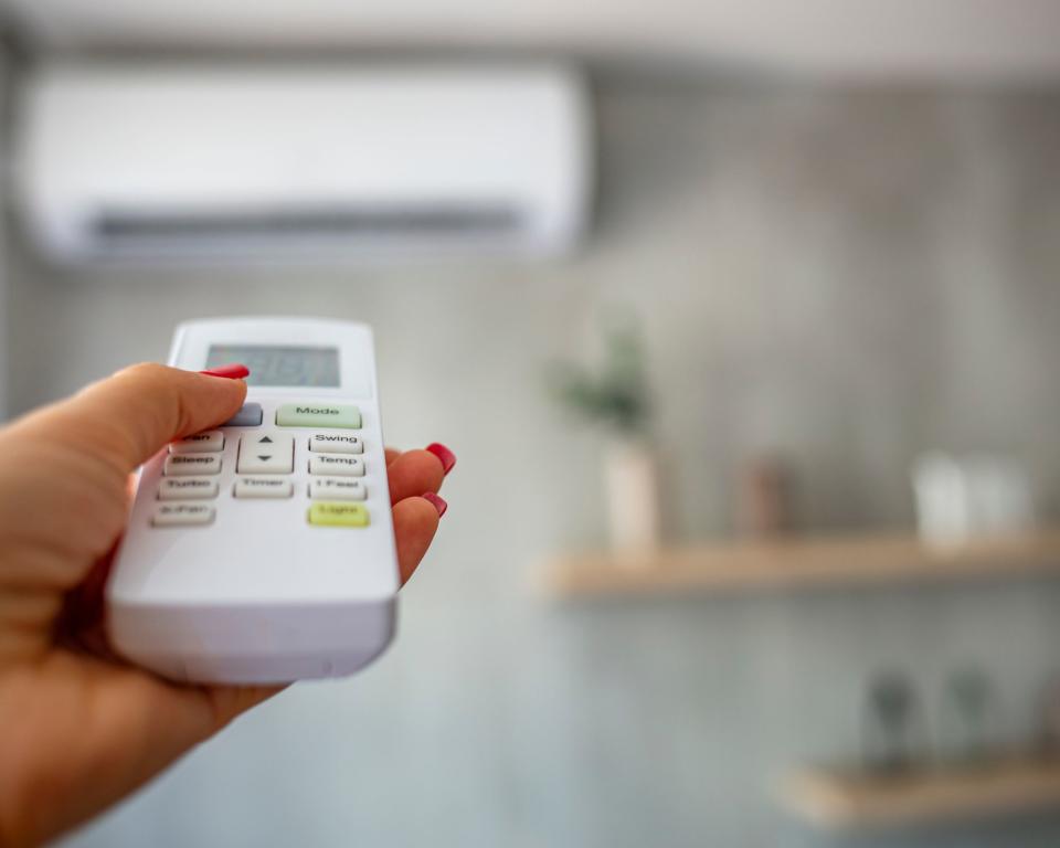 Bedroom with shelving unit woman holding AC controller pointing at AC unit on wall