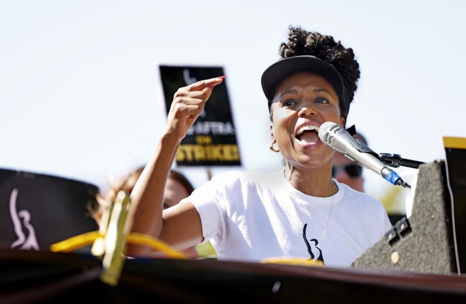 A woman speaks into a microphone and points with one finger