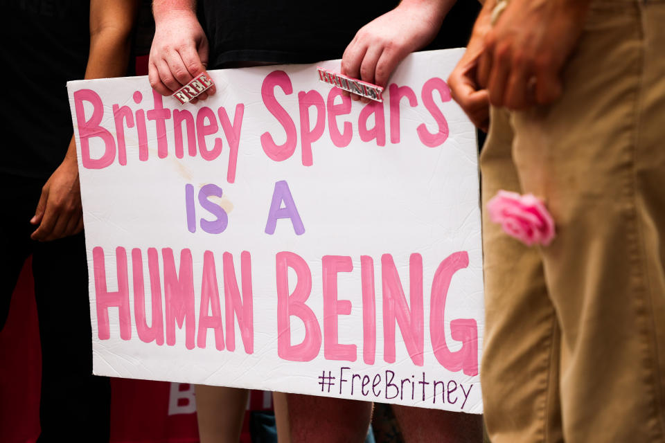 A person holding a sign that says "Britney Spears is a human being. #FreeBritney"