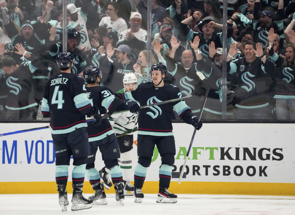 Dallas Stars center Wyatt Johnston (53) skates past as Seattle Kraken right wing Eeli Tolvanen, right, celebrates his goal with Justin Schultz (4) and Yanni Gourde (37) during the second period of Game 6 of an NHL hockey Stanley Cup second-round playoff series Saturday, May 13, 2023, in Seattle. (AP Photo/Lindsey Wasson)