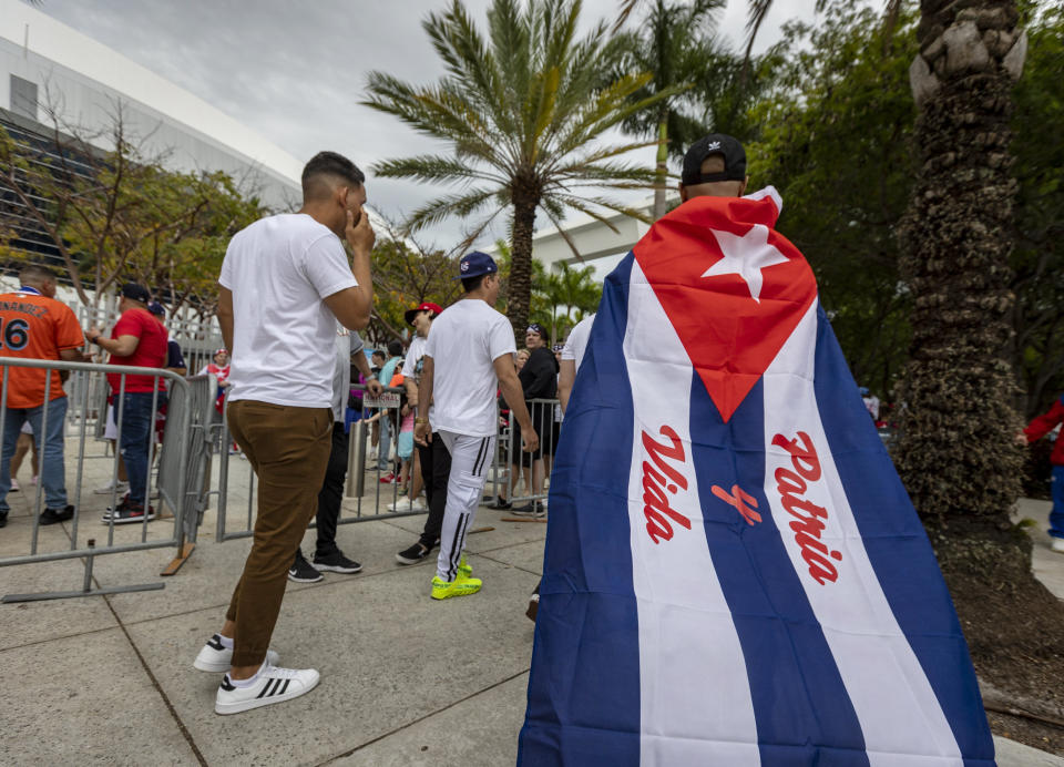 A man wearing a Cuban flag bearing the slogan of Patria y Vida walks toward the stadium before a World Baseball Classic game between between Cuba and the United States, Sunday, March 19, 2023, in Miami. (Jose A. Iglesias/Miami Herald via AP)