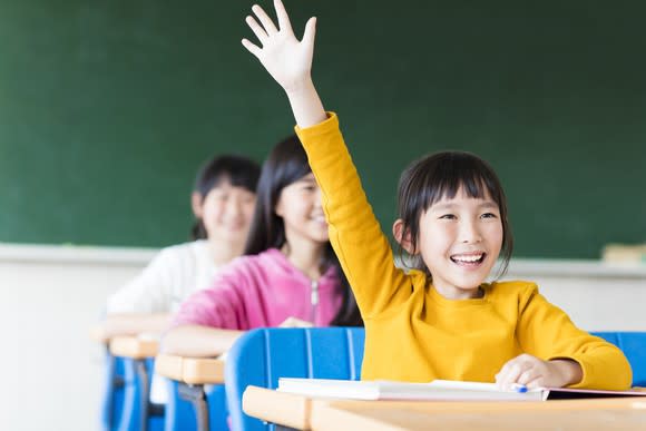 Girl in yellow shirt raising hand in class