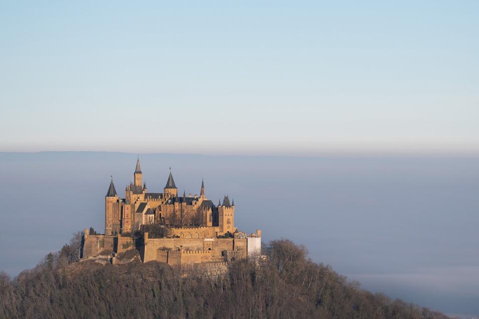 The sun shines on Hohenzollern Castle, while the land behind it is covered in fog.