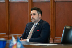 Sen. Blake Miguez sitting down. He is wearing a black suit jacket with a multi-colored tie and a red pocket square.