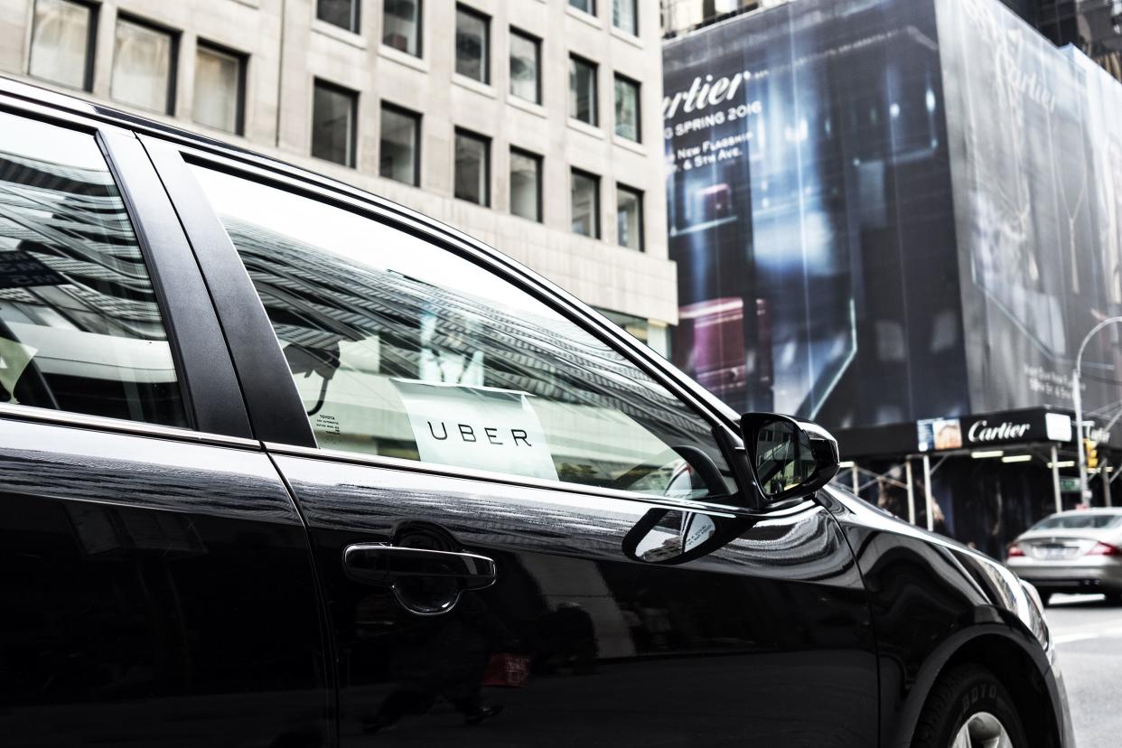 Uber sign in window of a black car, waiting for passengers on 5th Avenue in Manhattan, with Cartier store and other buildings in the background