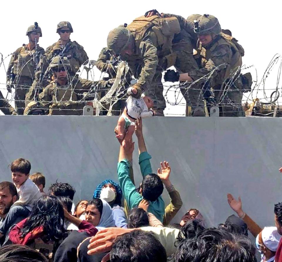 A U.S. Marine grabs an infant over a barbed-wire fence.