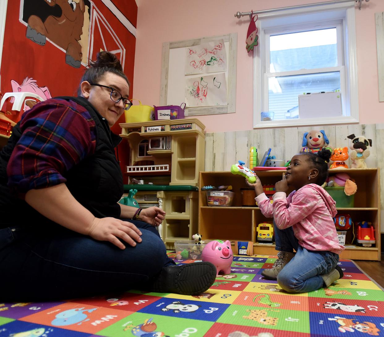 Kelly Cain plays with three-year-old Adrianna at Almost Home Day Care. The Newark day care center is at 50% capacity, with a waiting list of 60 kids, but doesn't have the staffing according to owner-operator Ginger Dehus.