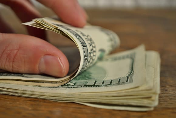 A hand counting a stack of $100 bills.