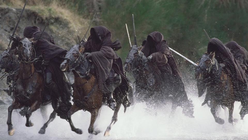 The hooded Nazgul ride their horses through a river in a scene from The Lord of the Rings: The Fellowship of the Ring.