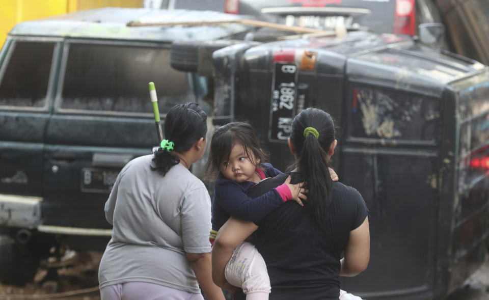 Residents stand near the wreckage of cars that were swept away by flood in Bekasi, West Java, Indonesia, Friday, Jan. 3, 2020. Severe flooding in greater Jakarta has killed scores of people and displaced tens of thousands others, the country's disaster management agency said. (AP Photo/Achmad Ibrahim)