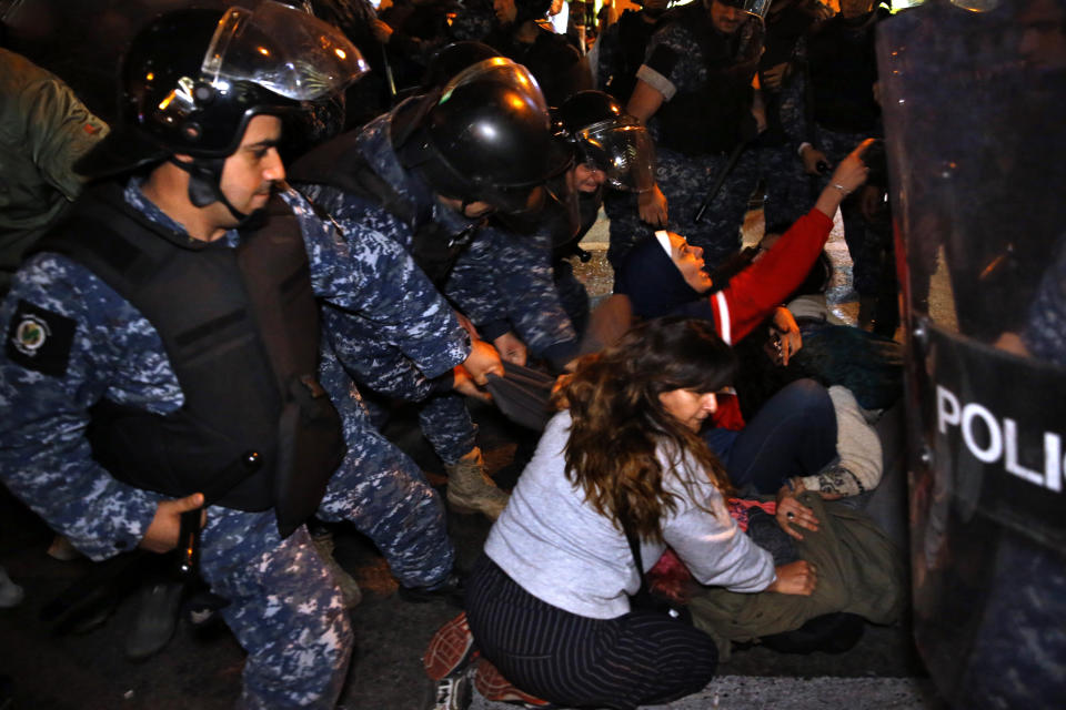 Protesters lie on a road, as they scream and hold each others while riot police try to remove them and open the road, in Beirut, Lebanon, Wednesday, Dec. 4, 2019. Protesters have been holding demonstrations since Oct. 17 demanding an end to corruption and mismanagement by the political elite that has ruled the country for three decades. (AP Photo/Bilal Hussein)