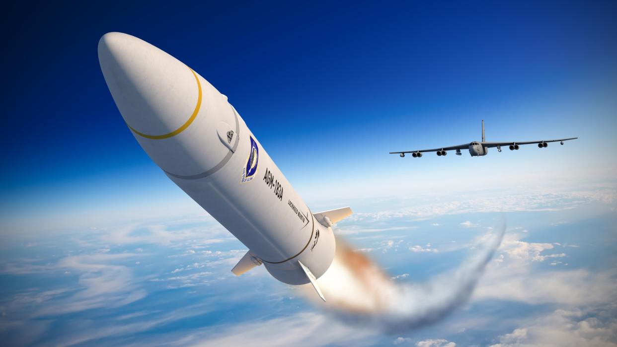  in an illustration, a missile flies above the earth and clouds. far behind is a large military plane that deployed the missile 