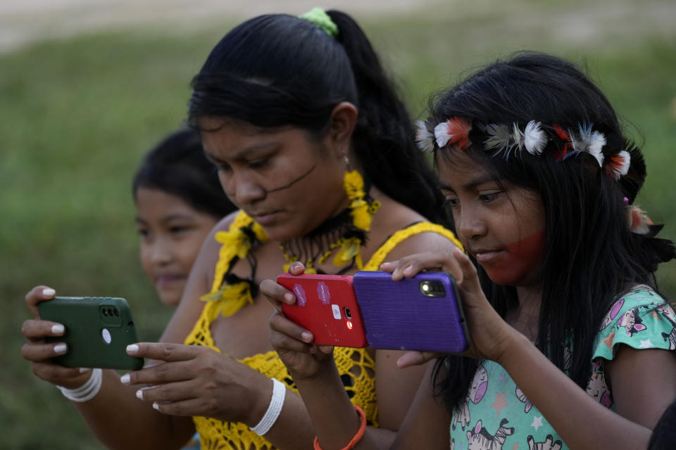 An Indigenous Tembe mother and daughters take photos on their smartphones outside a school in the Tenetehar Wa Tembe village, located in the Alto Rio Guama Indigenous territory of the Paragominas municipality in the Para state of Brazil, Tuesday, May 30, 2023. (AP Photo/Eraldo Peres)