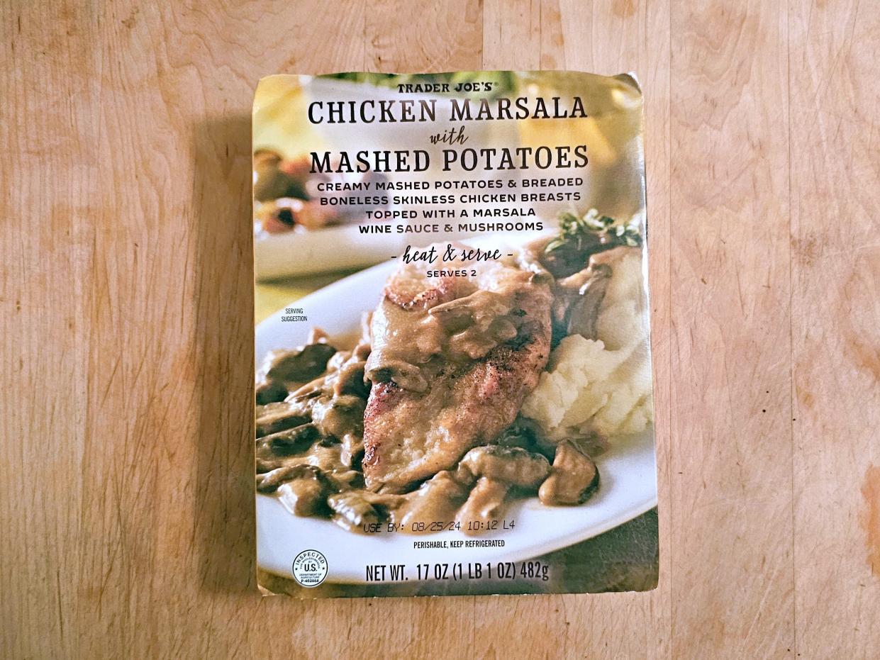 A box of Trader Joe's chicken Marsala with mashed potatoes against a wooden background.